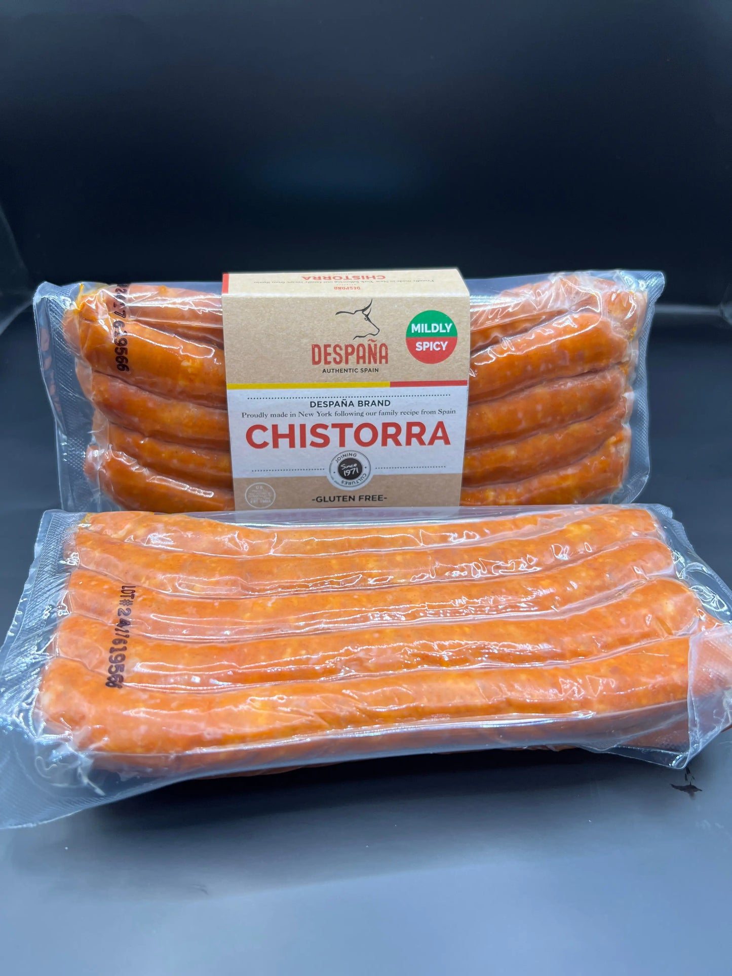 Two vacuum-sealed packs of mildly spicy CHISTORRA sausages, bright reddish-orange in color, displayed on a dark surface.