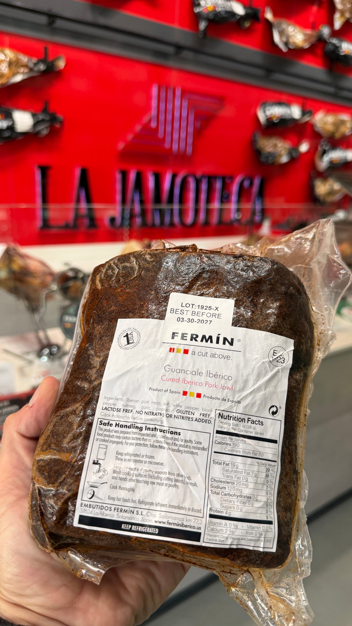 IBERICO GUANCCIALE (HALF) vacuum-sealed cured pork cheek held in hand with product label visible at a Spanish specialty store counter