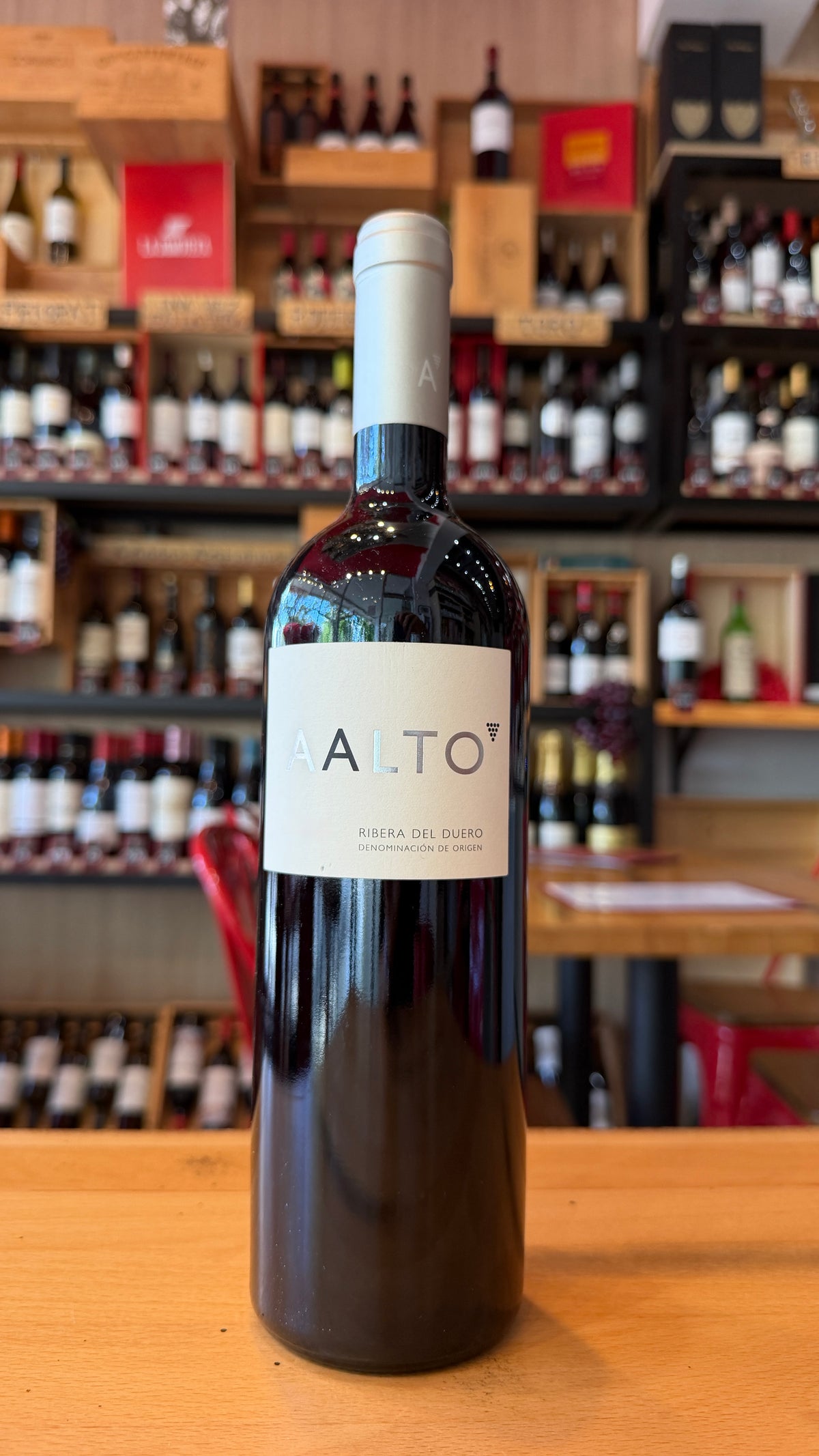 AALTO, RIBERA DEL DUERO red wine bottle displayed on a wooden counter in a Spanish specialty store with wine shelves in the background