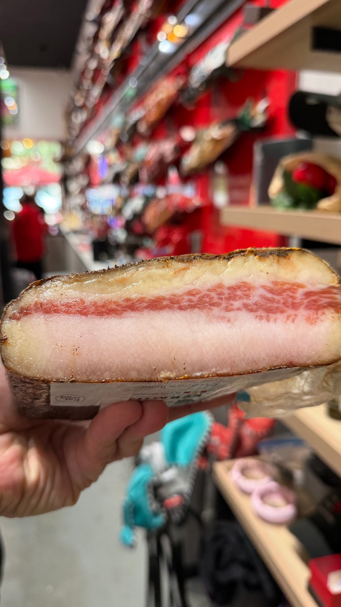IBERICO GUANCCIALE (HALF) showing rich marbling and a golden cured rind held in hand at a Spanish specialty store